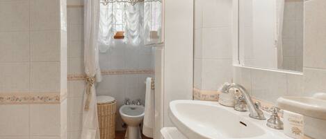 Une salle de bain avec un lavabo blanc, un miroir, un bidet et un rideau de douche.