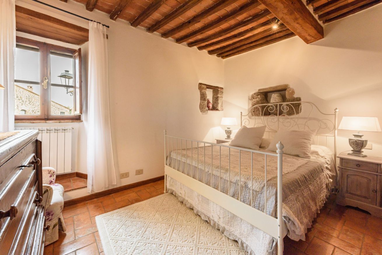 Une chambre avec un plafond en bois, un lit avec un cadre en métal, une table de chevet avec une lampe et une commode.