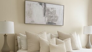 A neatly arranged bedroom with a large bed, multiple pillows, two bedside tables with lamps, and a single artwork on the wall.