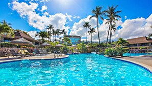 A swimming pool with lounge chairs and palm trees, surrounded by resort buildings.