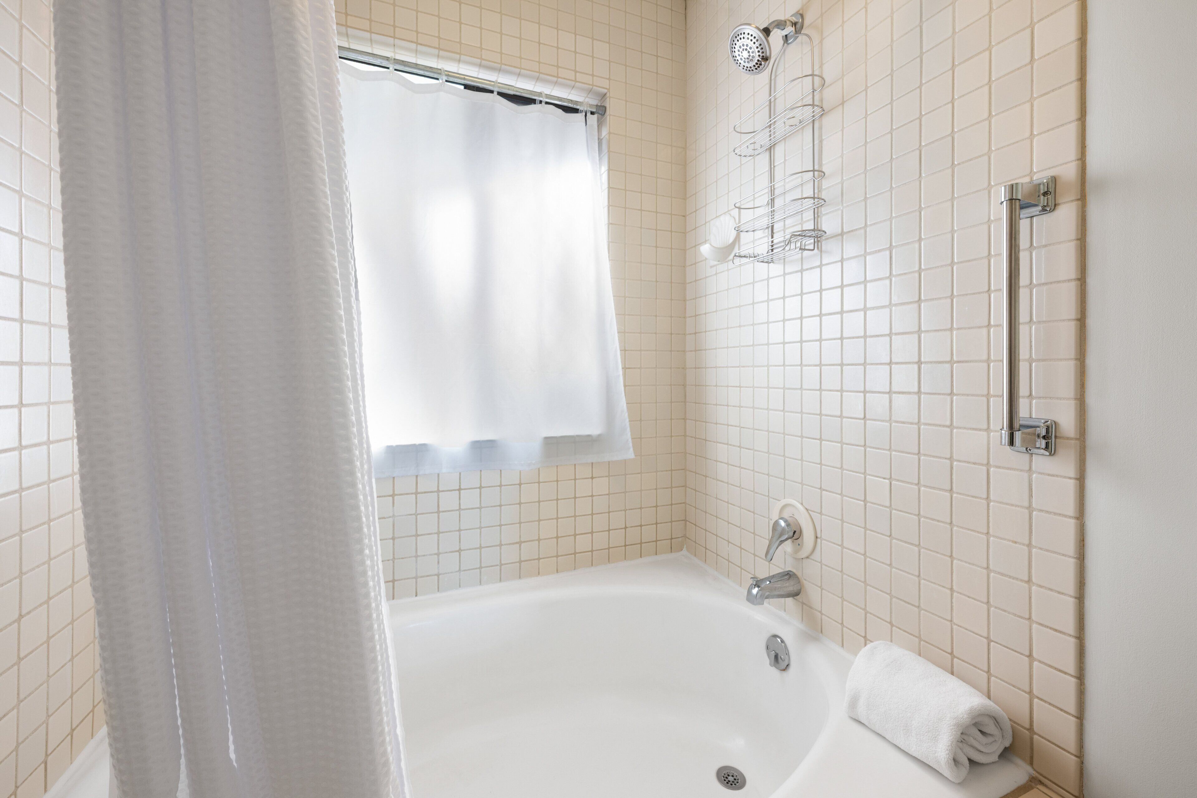 Une salle de bain équipée d’une baignoire, d’un rideau de douche, d’un porte-serviettes et d’une barre d’appui.