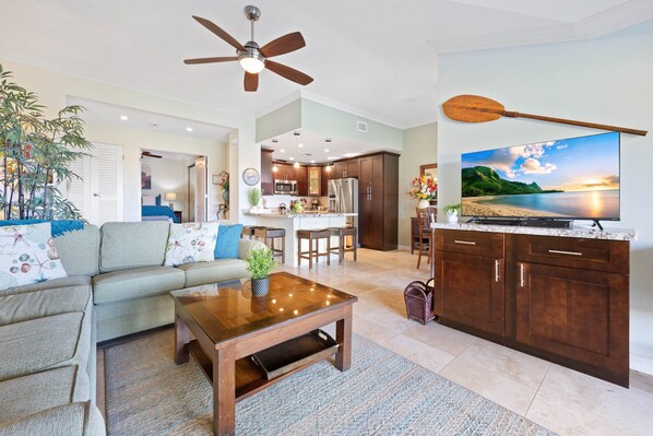 A living room with a sofa, coffee table, and a television on a wooden cabinet. - 2bd chic Island elegance and comfort (Lahaina)