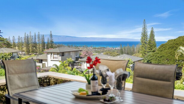 A dining table with chairs and a view of the ocean and hills.
