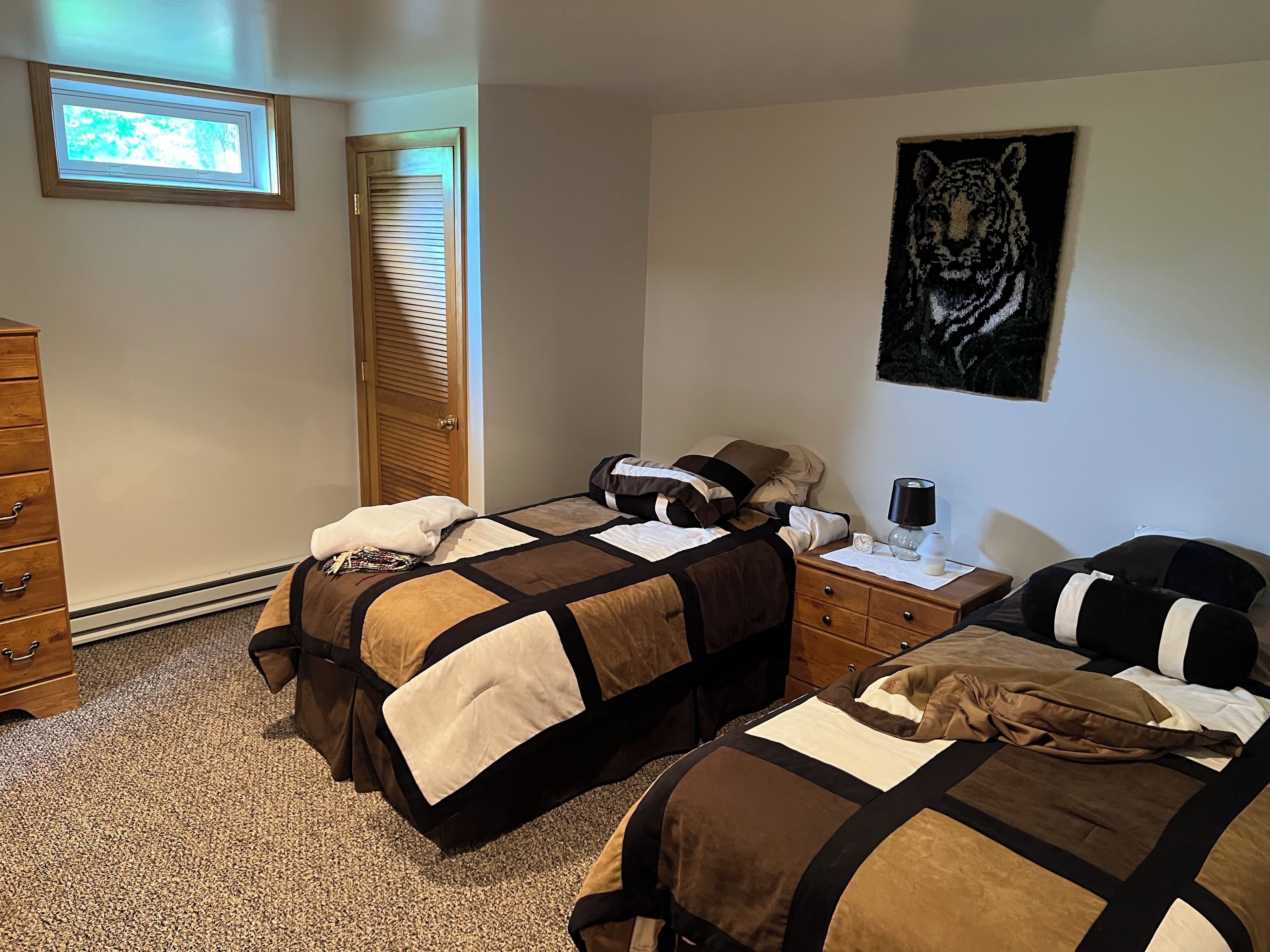 Un dormitorio con dos camas, un aparador, una mesita de noche, una ventana con persianas y una obra de arte con estampado de tigre en la pared.