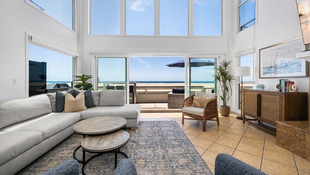 A spacious living area with a large sofa, a round coffee table, and a wicker chair. - Spacious Oceanfront Home Near Newport Pier (Newport Beach)
