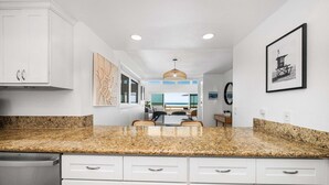 A kitchen with granite countertops, white cabinetry, and a dining area with a view of the ocean. - Spacious Oceanfront Home Near Newport Pier (Newport Beach)