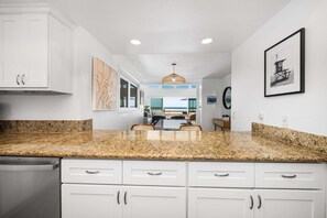 A kitchen with granite countertops, white cabinetry, and a dining area with a view of the ocean.