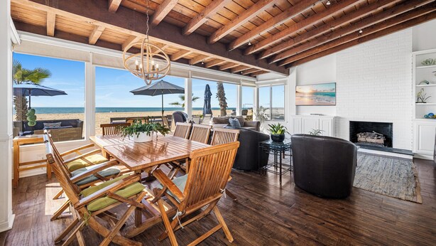 A spacious living area with a wooden dining table, comfortable seating, and a view of the beach. - Luxurious Oceanfront Home with Incredible Views (Newport Beach)