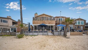 A beachfront property with a covered patio, outdoor seating, and a sandy beach area. - Luxurious Oceanfront Home with Incredible Views (Newport Beach)