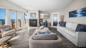 A spacious living room with a fireplace, a large sofa, and a view of the beach through glass doors. - Luxurious Oceanfront Home with Incredible Views (Newport Beach)