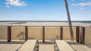 A beach view from a balcony with a palm tree, a pool, and a clear sky. - Luxurious Oceanfront Home with Incredible Views (Newport Beach)