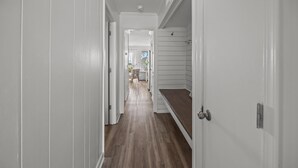 Un couloir étroit, doté d’un plancher en bois et de murs blancs, mène à une pièce offrant une vue sur l’extérieur.