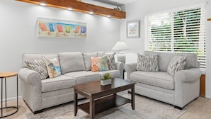 A living room with two grey sofas, a wooden coffee table, a small plant, and a painting on the wall. - 1-Bedroom Rental w/ Ocean Views (Palm Beach Shores)