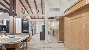 A spacious kitchen with wooden beams, a dining area with a large table, and a view into a living room. - Beachfront Studio w/ Ocean Views (Palm Beach Shores)