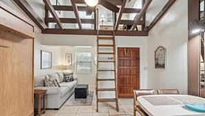 A spacious living area with a high ceiling, wooden beams, a loft bedroom, a dining area, and a staircase. - Beachfront Studio w/ Ocean Views (Palm Beach Shores)