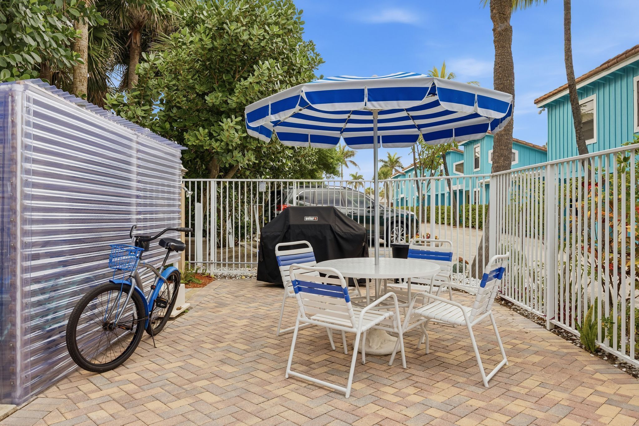 A patio area with a table and chairs, a covered grill, a bicycle, and a fence.