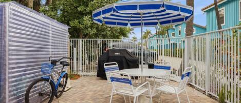 A patio area with a table and chairs, a covered grill, a bicycle, and a fence.