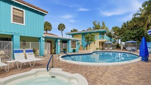 A pool area with a hot tub, lounge chairs, and a building with a blue exterior.