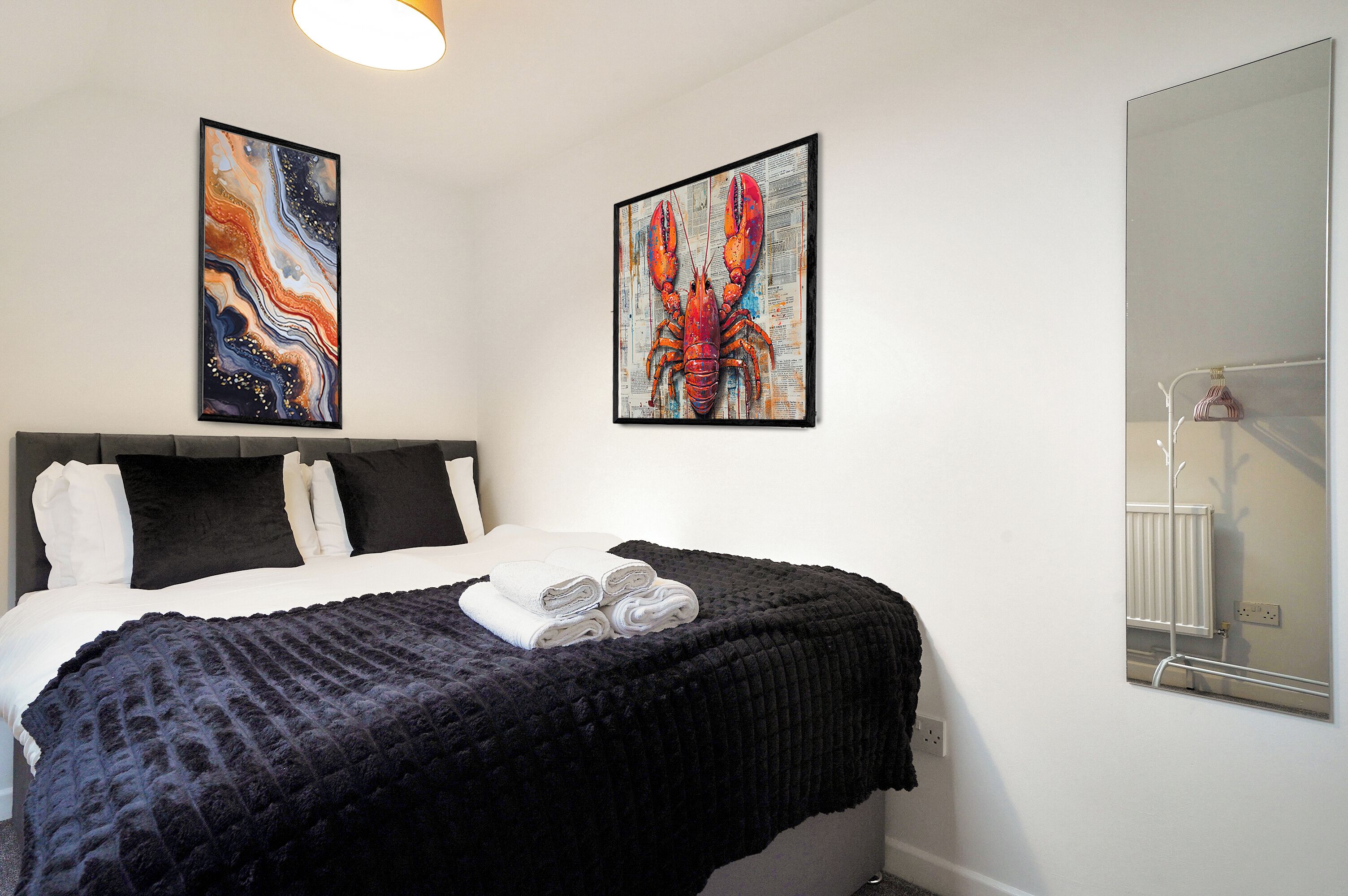 Une chambre d’hôtel avec un lit, deux œuvres d’art encadrées, un grand miroir et un radiateur.