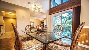 Un coin repas avec une table en verre entourée de chaises en osier agrémentées de coussins à motifs.