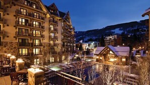 Un hotel a più piani con balconi, una zona piscina e vista su una montagna innevata.