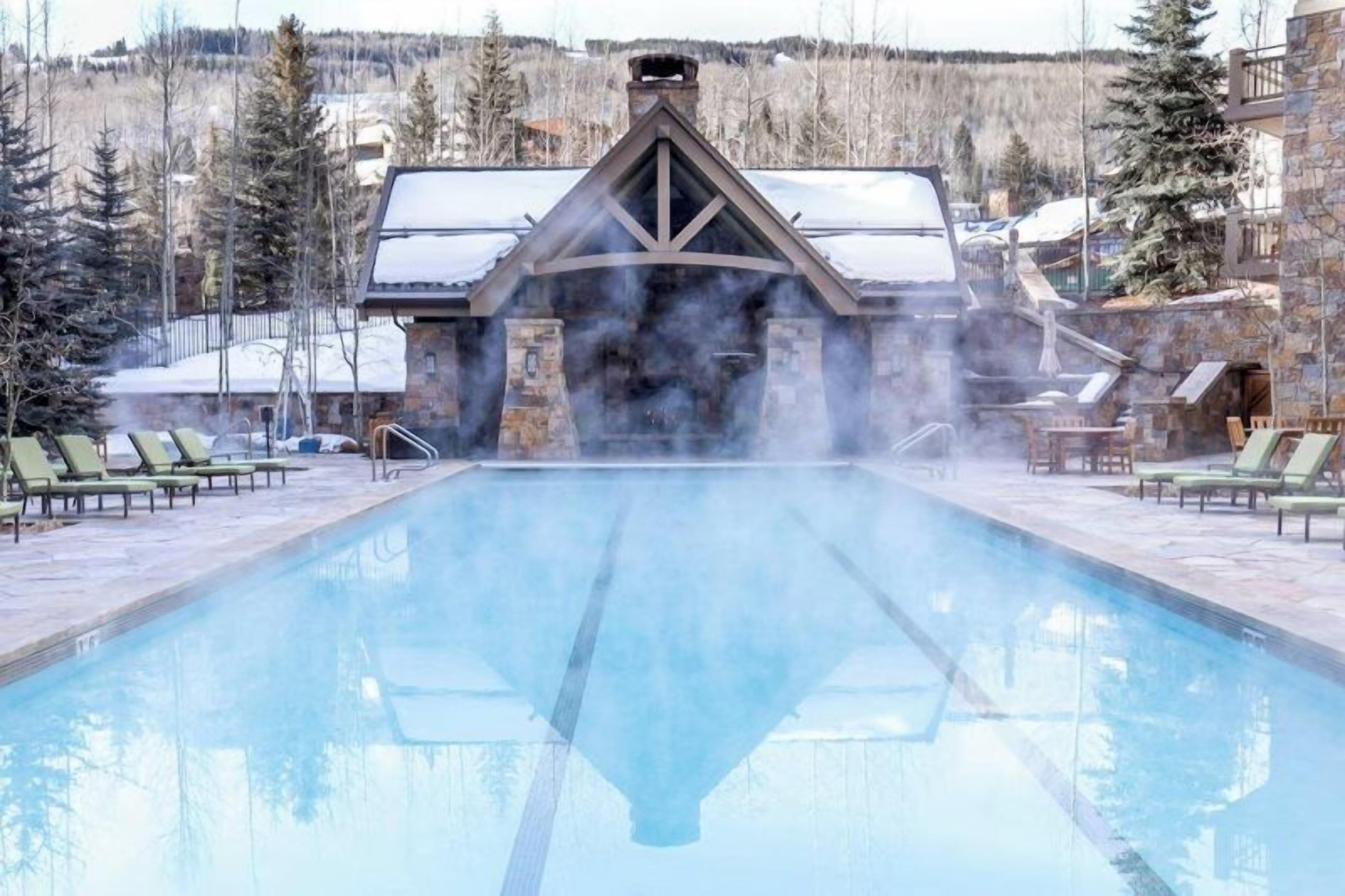 A pool area with lounge chairs and a stone building with a chimney emitting steam.