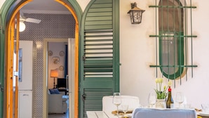 An open doorway leading to a dining area with a table set for two, a green shutter door, and a wall-mounted lantern. - Villa Valmar - Villa with a view (Taormina)