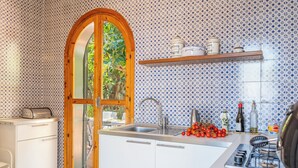 A kitchen with a wooden arch door, white cabinets, a sink, and a stove. There are tomatoes on the counter and a bottle of olive oil. - Villa Valmar - Villa with a view (Taormina)