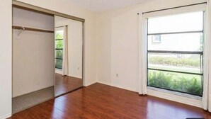 A room with hardwood flooring, a sliding door closet, and a large window with a view of greenery.