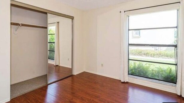 A room with hardwood flooring, a sliding door closet, and a large window with a view of greenery.