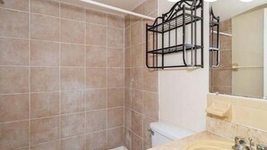 A bathroom with beige tiles, a white toilet, a sink with a mirror, and a black towel rack.