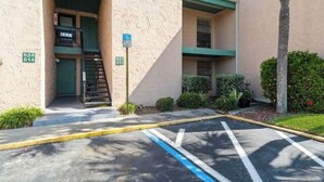 A parking lot with marked spaces, a building entrance with a ramp, and a green sign indicating a handicap parking spot.