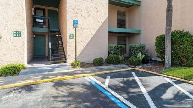 A parking lot with marked spaces, a building entrance with a ramp, and a green sign indicating a handicap parking spot.
