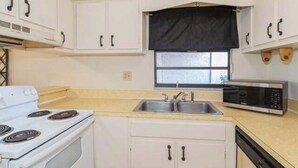 A compact kitchen with white cabinets, a double sink, a stove, and a microwave.