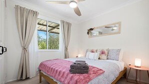 A bedroom with a bed, a bedside table with a lamp, a window with curtains, and a ceiling fan. - Urban Connection Farm (Eagleton)