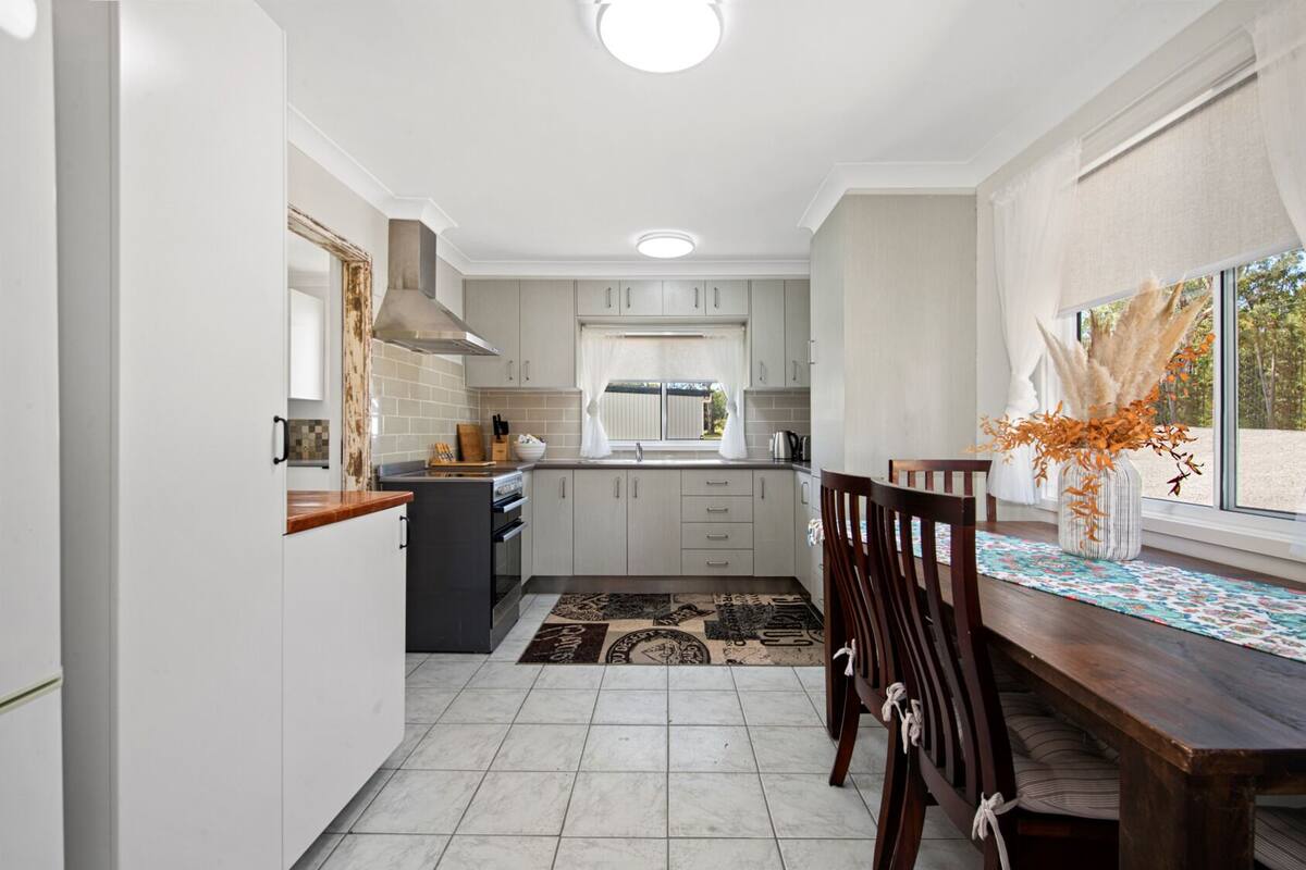 A compact kitchen with white cabinets, a dining table with chairs, and a window with a view of the outdoors.