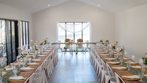 A long dining table set for a formal event with white chairs, glassware, and floral centerpieces. - Urban Connection Farm (Eagleton)