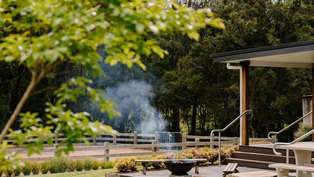 A fire pit area with a bench and a covered seating area, surrounded by a wooden fence and greenery. - Urban Connection Farm (Eagleton)