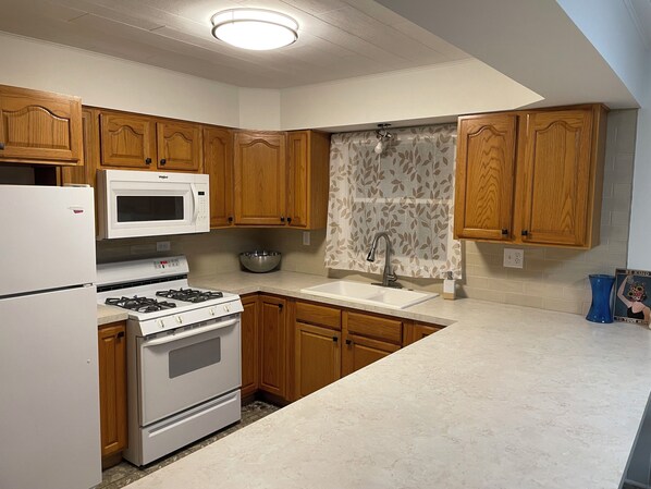 A kitchen with wooden cabinets, a white refrigerator, a microwave, a stove, and a sink.
