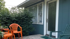 Una terraza de madera con mobiliario exterior, una puerta corrediza de vidrio y una silla verde.