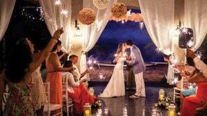 Una ceremonia de boda con invitados sentados en sillas, una pareja besándose y luces decorativas.