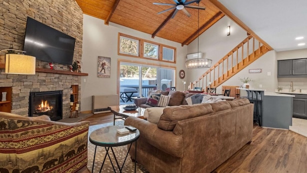 A spacious living room with a stone fireplace, a large brown sofa, and a television mounted on the wall.