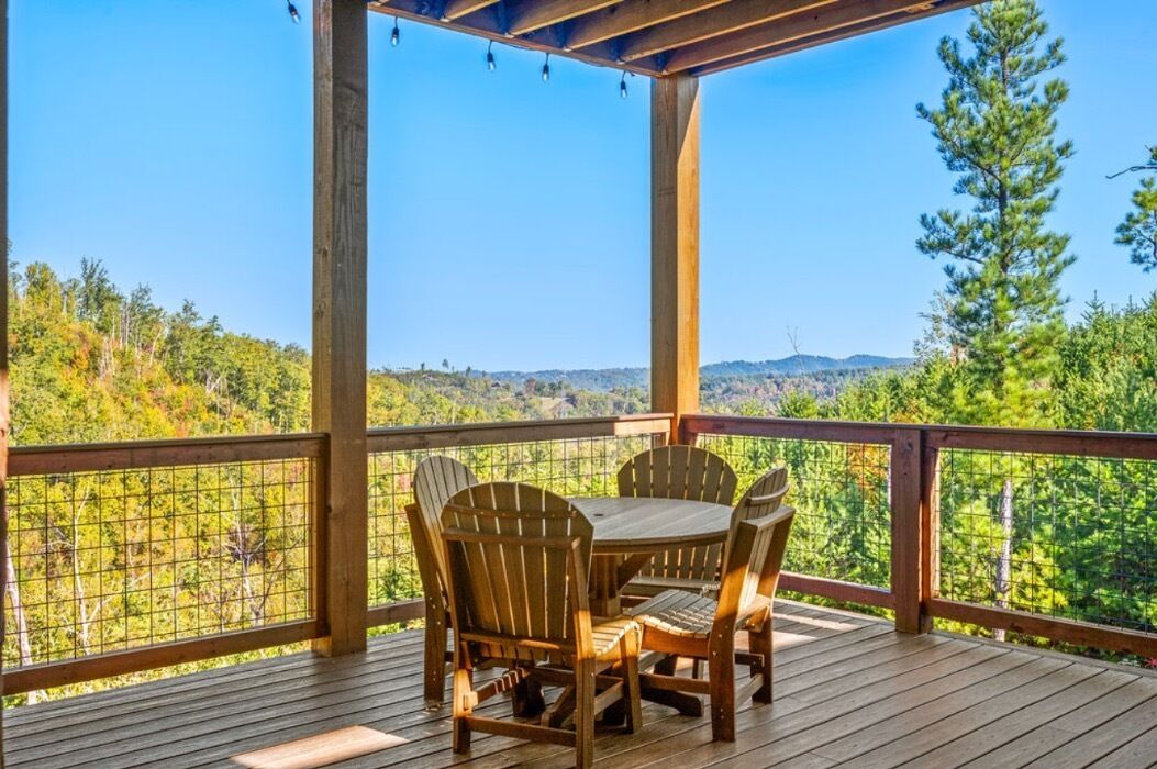 A wooden deck with a table and chairs, overlooking a forested landscape.
