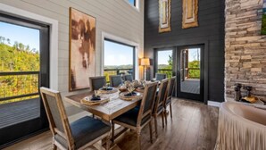 A dining area with a wooden table set for six, large windows, and a stone wall.