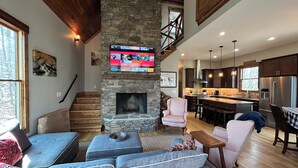Un salón espacioso con chimenea de piedra, un televisor grande montado encima y una zona de estar acogedora con sofá y sillones.