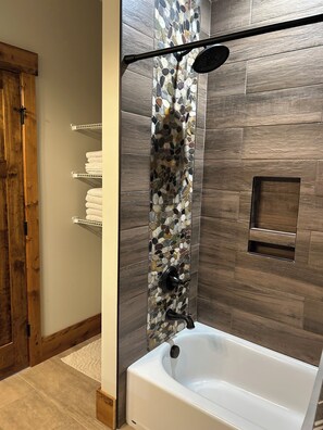 Ein modernes Badezimmer mit einer freistehenden Badewanne, einer Dusche mit Wand aus Steinmosaik und Holzboden.