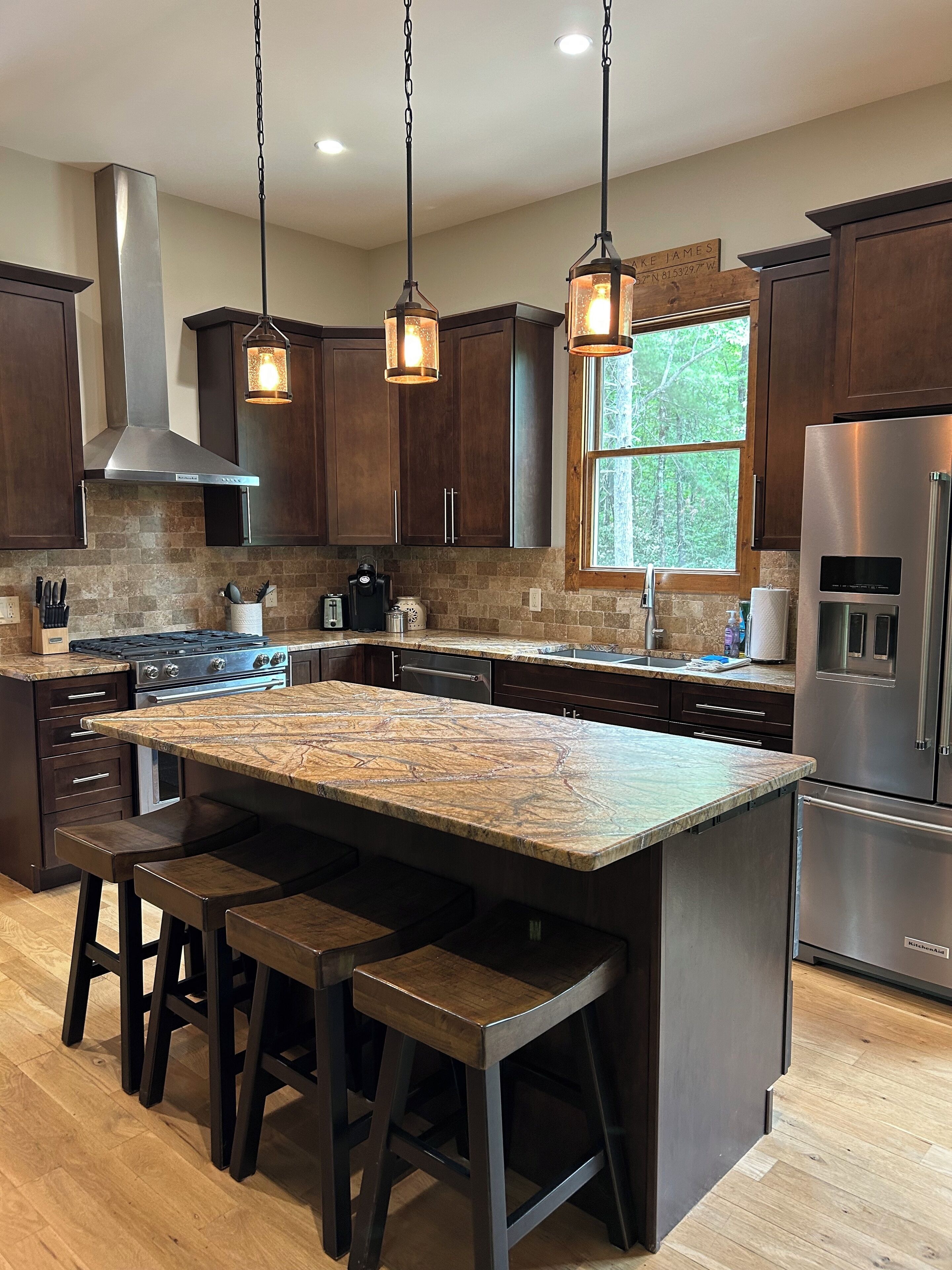 A modern kitchen with dark wood cabinets, a large island with bar stools, stainless steel appliances, and pendant lighting.