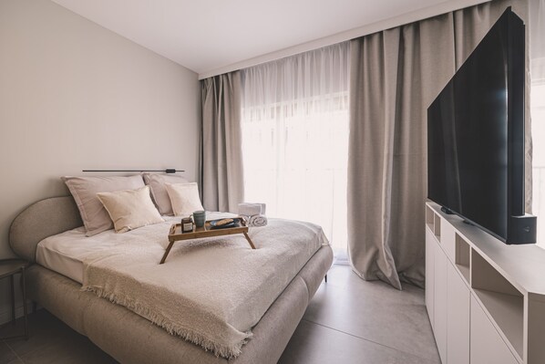A modern bedroom with a large bed, a bedside table, a flat-screen TV, and a window with curtains. - Casa Przestronne Studio z Balkonem Klimatyzacja Opera Nova Star wka (Bydgoszcz)