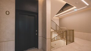 A modern elevator with a dark door, a staircase with a metal railing, and a lighted exit sign. - Casa Przestronne Studio z Balkonem Klimatyzacja Opera Nova Star wka (Bydgoszcz)