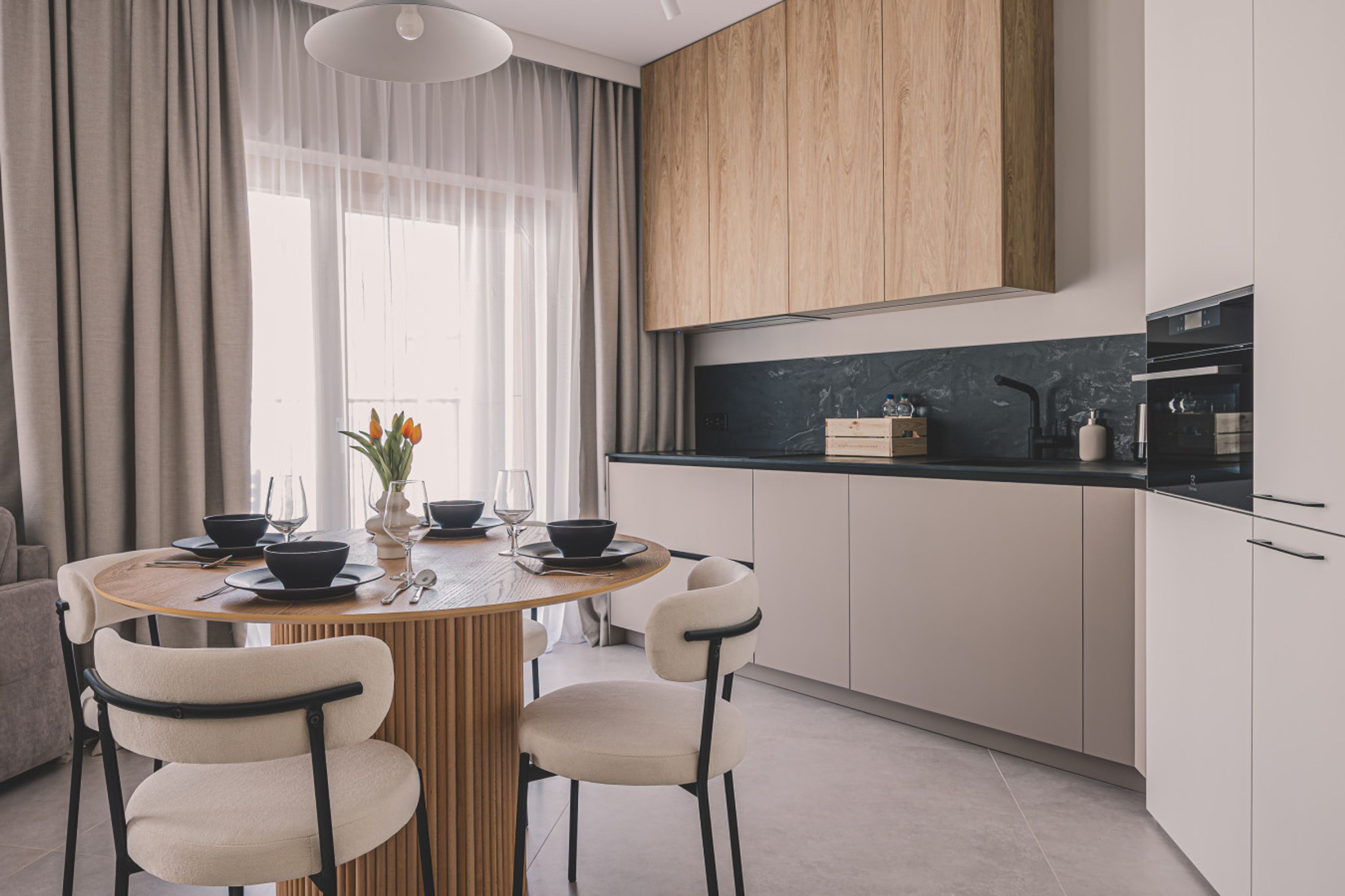 Een moderne keuken met een houten eettafel, witte stoelen en een zwart aanrecht.
